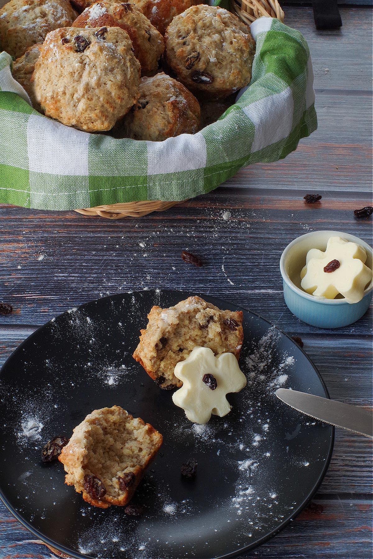Healthy Irish Soda Bread Muffin, split in half, on a black plate, with a shamrock butter leaning against one half of the muffin.