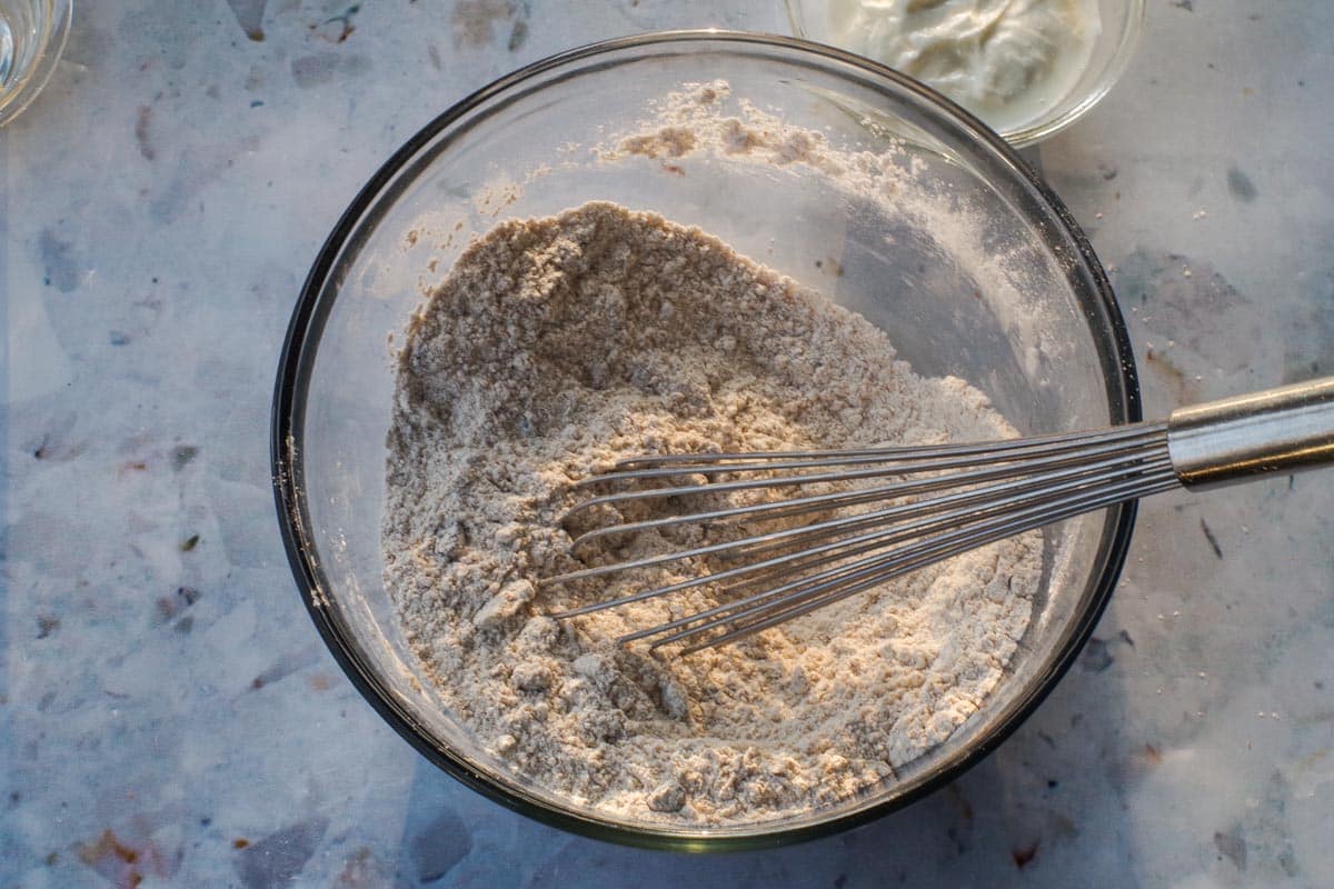 Dry ingredients mixed together with raisins with whisk in glass bowl.