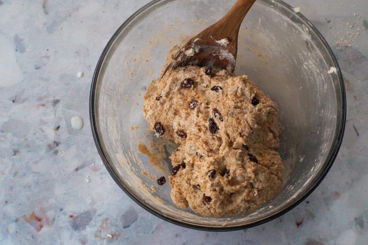 Wet ingredients stirred into dry ingredients with a wooden spoon in a large glass bowl.