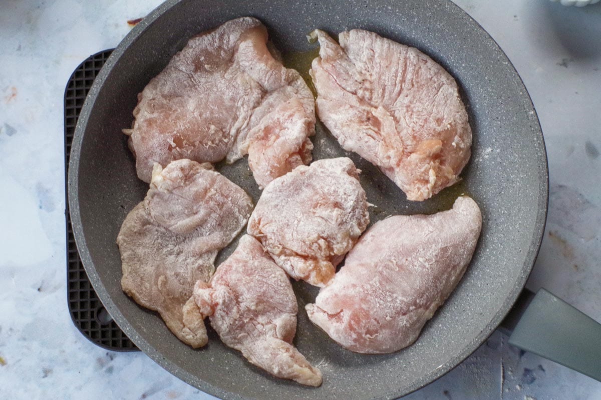 Coated raw chicken breasts in a blue pan