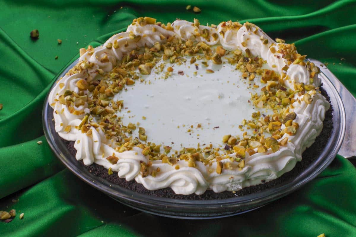 A whole Healthy High Protein Pistacho Pie on a green background with a pie server beside it.