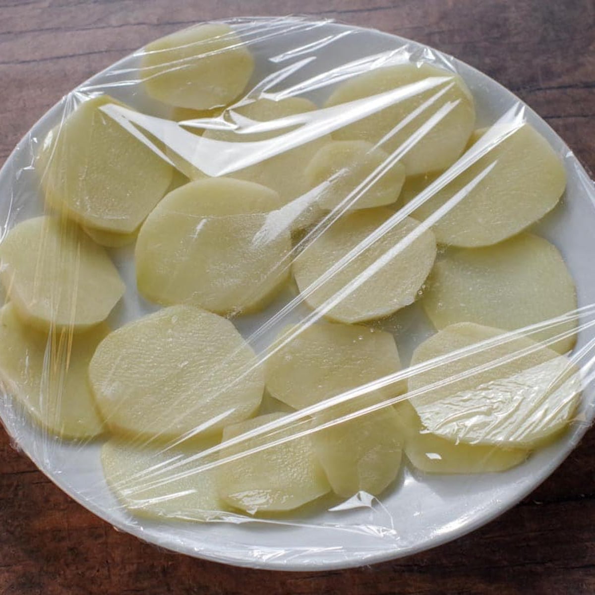 Potatoes on a plate, covered in plastic wrap.