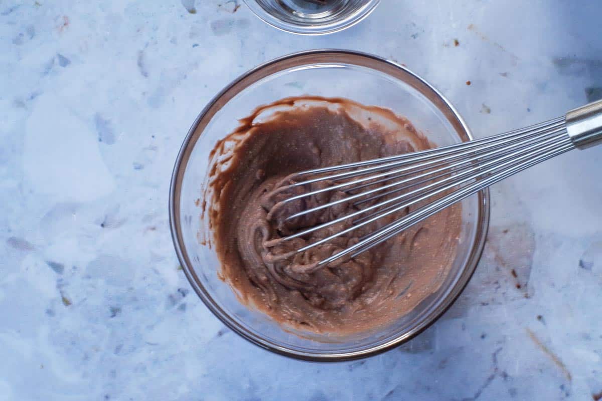 Mascarpone cheese, chocolate pudding and Kahlua mixed together in glass bowl with a metal whisk.