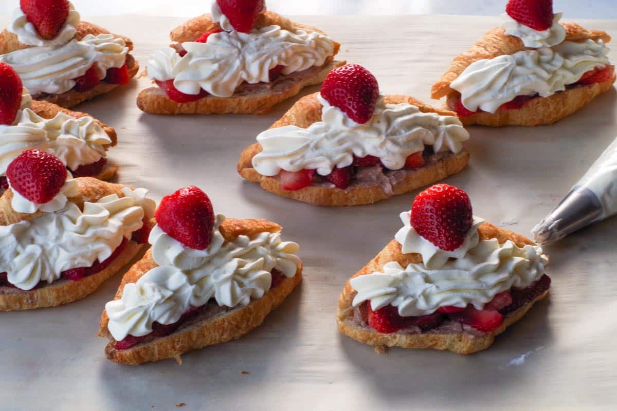 A dollop of whipped cream piped onto the top of the croissant with a ½ a strawberry placed on top of that.