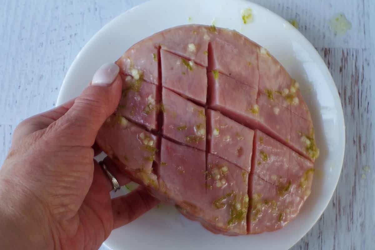 Hand holding up a ham steak, showing marinade in grooves.