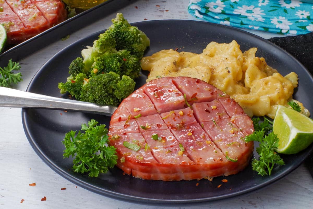 Air Fryer Ham Steak on a black plate with broccoli and scalloped potatoes