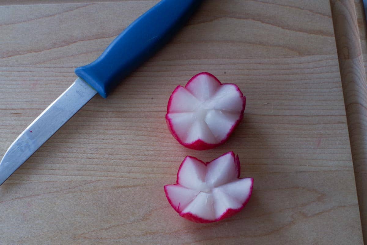 2 radish flower (tulips) on a wooden cutting board with a paring knife.