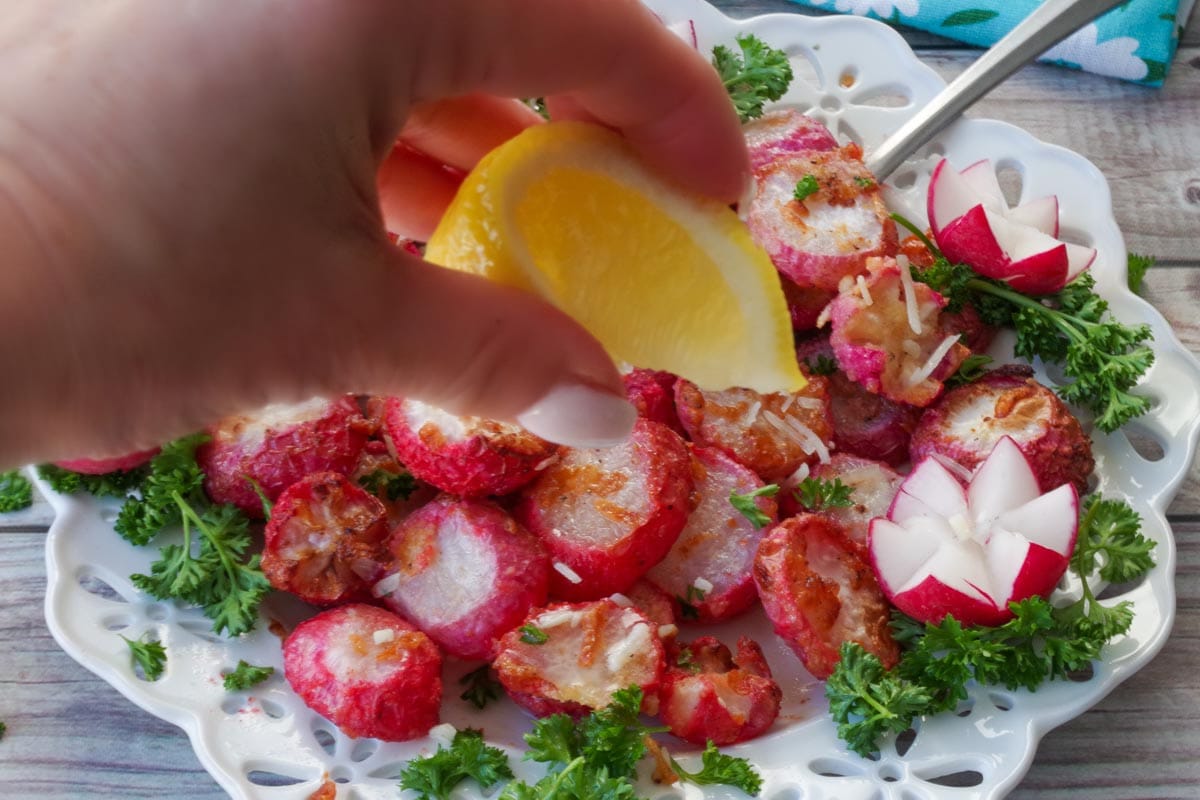 Plate of air fryer roasted radishes with a fresh lemon being squeezed over it.
