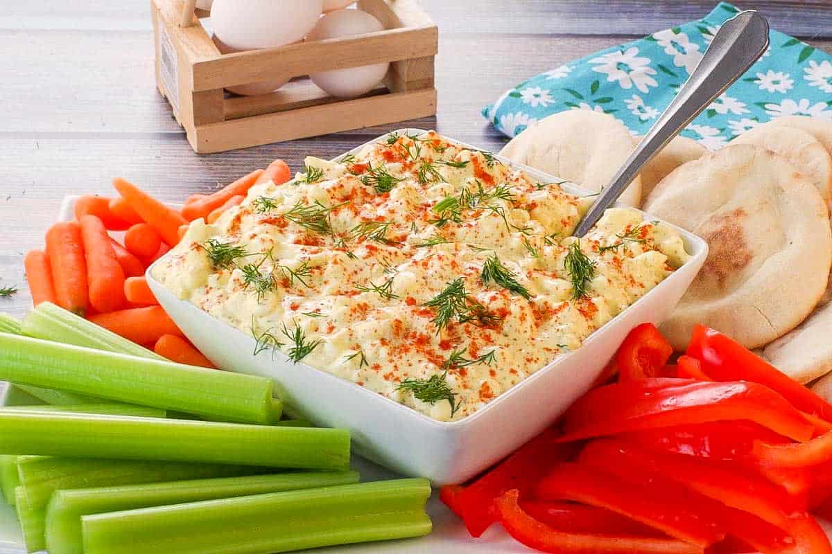 Dill Deviled Egg Dip in the mdidle of a platter of vegetables, with eggs in the background.
