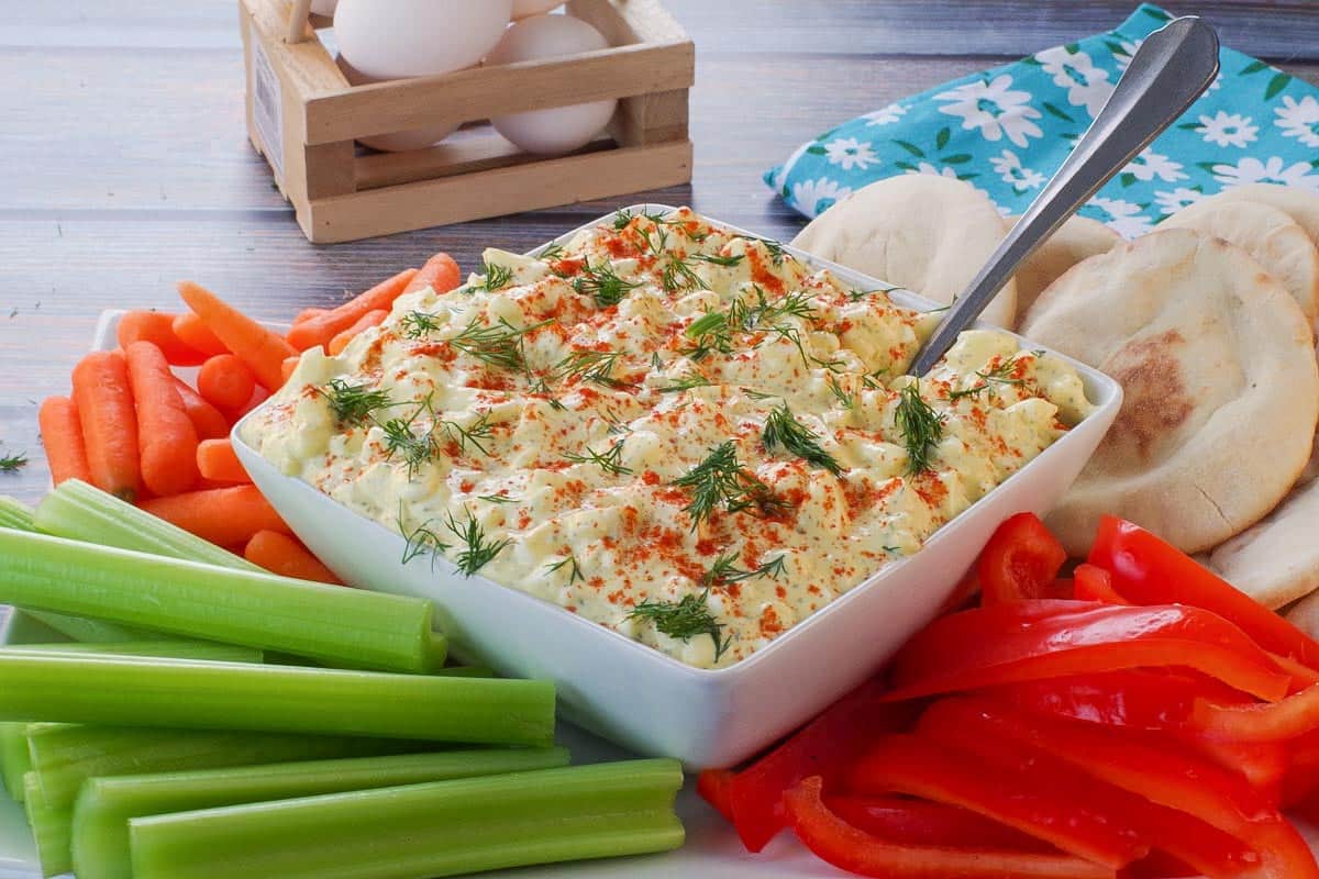 Dill Deviled Egg Dip in the mdidle of a platter of vegetables, with eggs in the background.