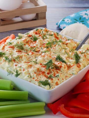 Dill Deviled Egg Dip in the mdidle of a platter of vegetables, with eggs in the background.