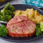 Air Fryer Ham Steak on a black plate with broccoli and scalloped potatoes
