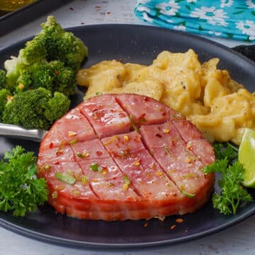 Air Fryer Ham Steak on a black plate with broccoli and scalloped potatoes
