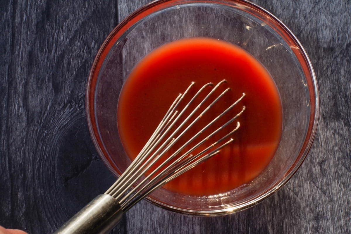 Ketchup, brown sugar and water whisked together in a medium glass bowl with a large metal whisk.