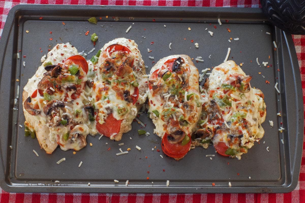 4 pieces of White Pizza Chicken on a sheet pan, garnished with red pepper flakes and additional parmesan.