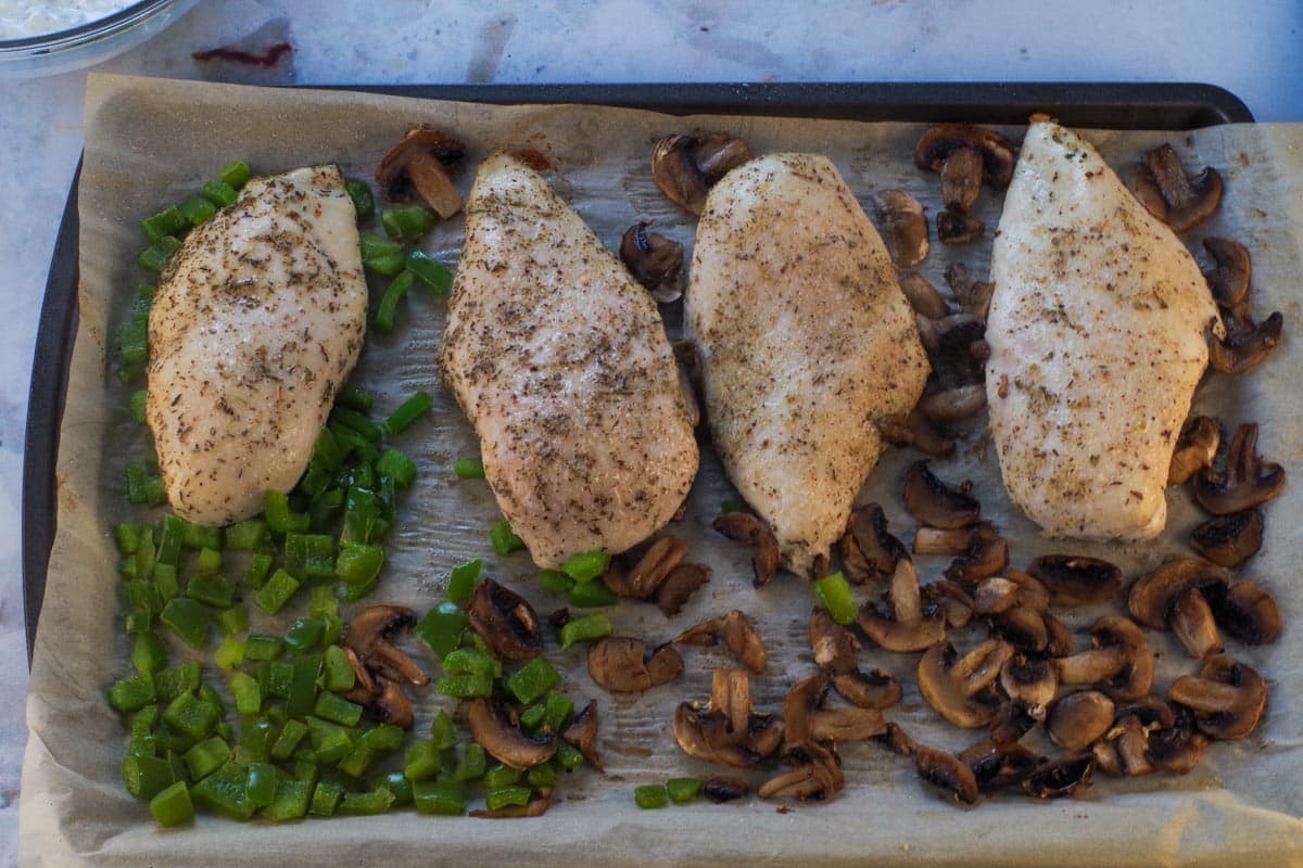 Semi-cooked chicken with cooked vegetables on a sheet pan.