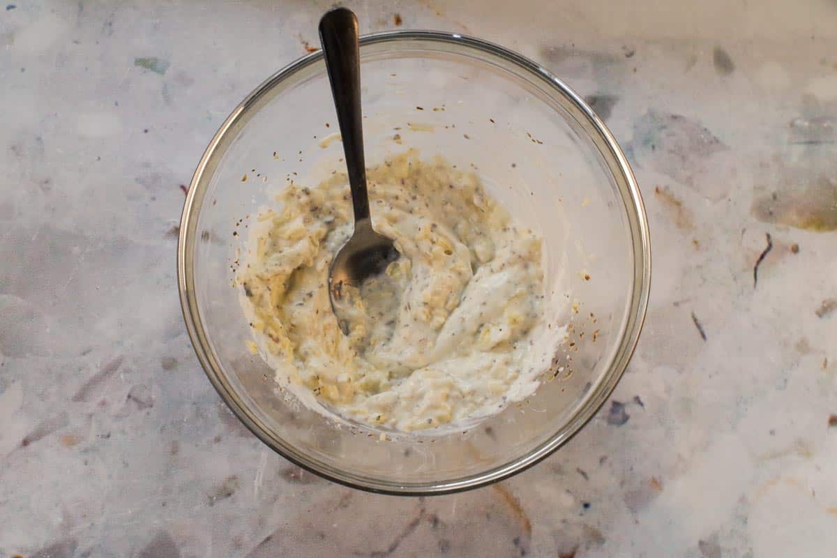 White sauce ingredients mixed together in glass bowl with spoon.