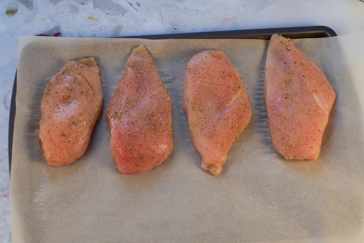 Raw chicken rubbed with rub mixture on parchment covered sheet pan.