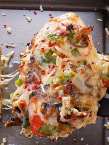 Healthy Sheet Pan Pizza Chicken being lifted off a sheet pan with a black spatula.