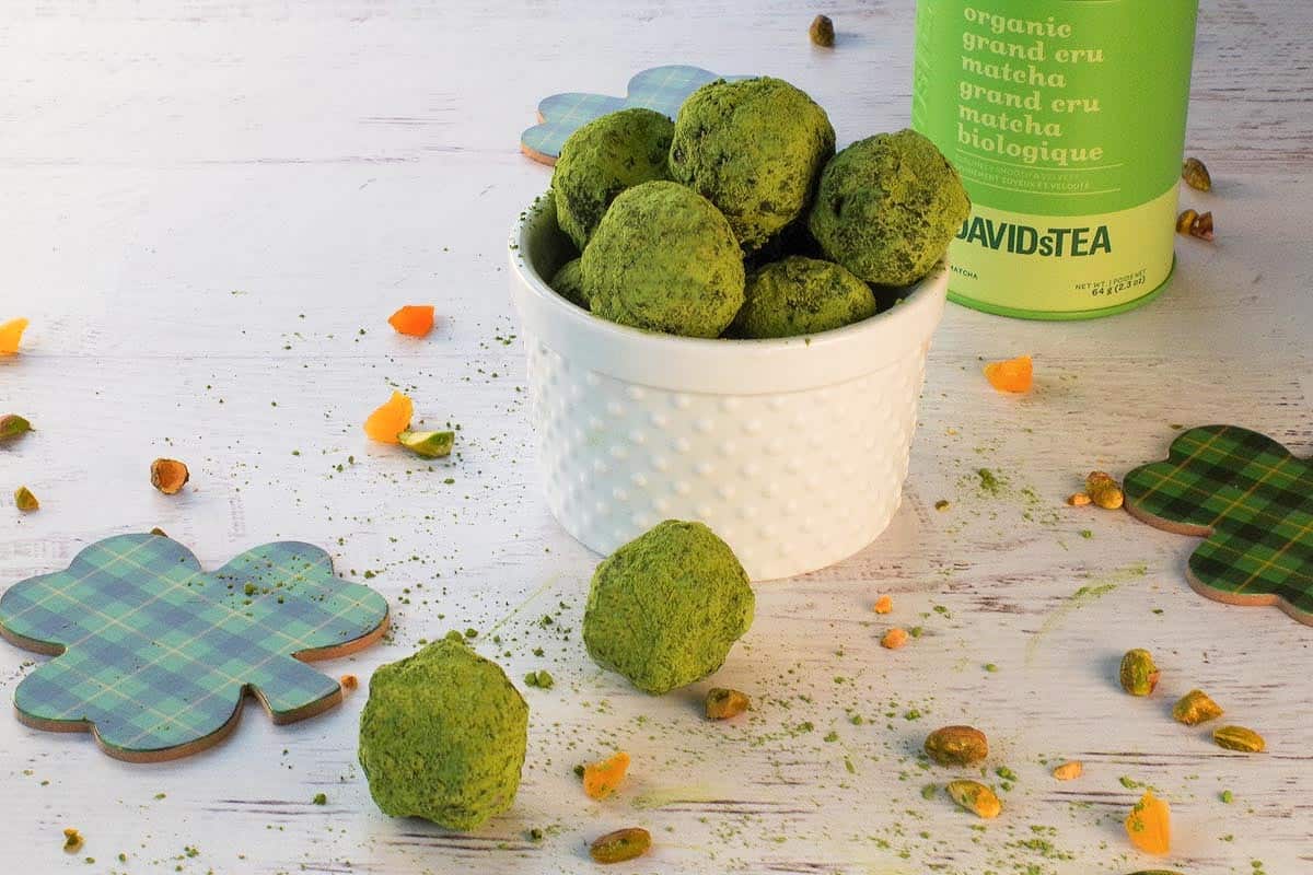 2 matcha pistachio energy bites on a piece of parchment with more in a small bowl in the background.