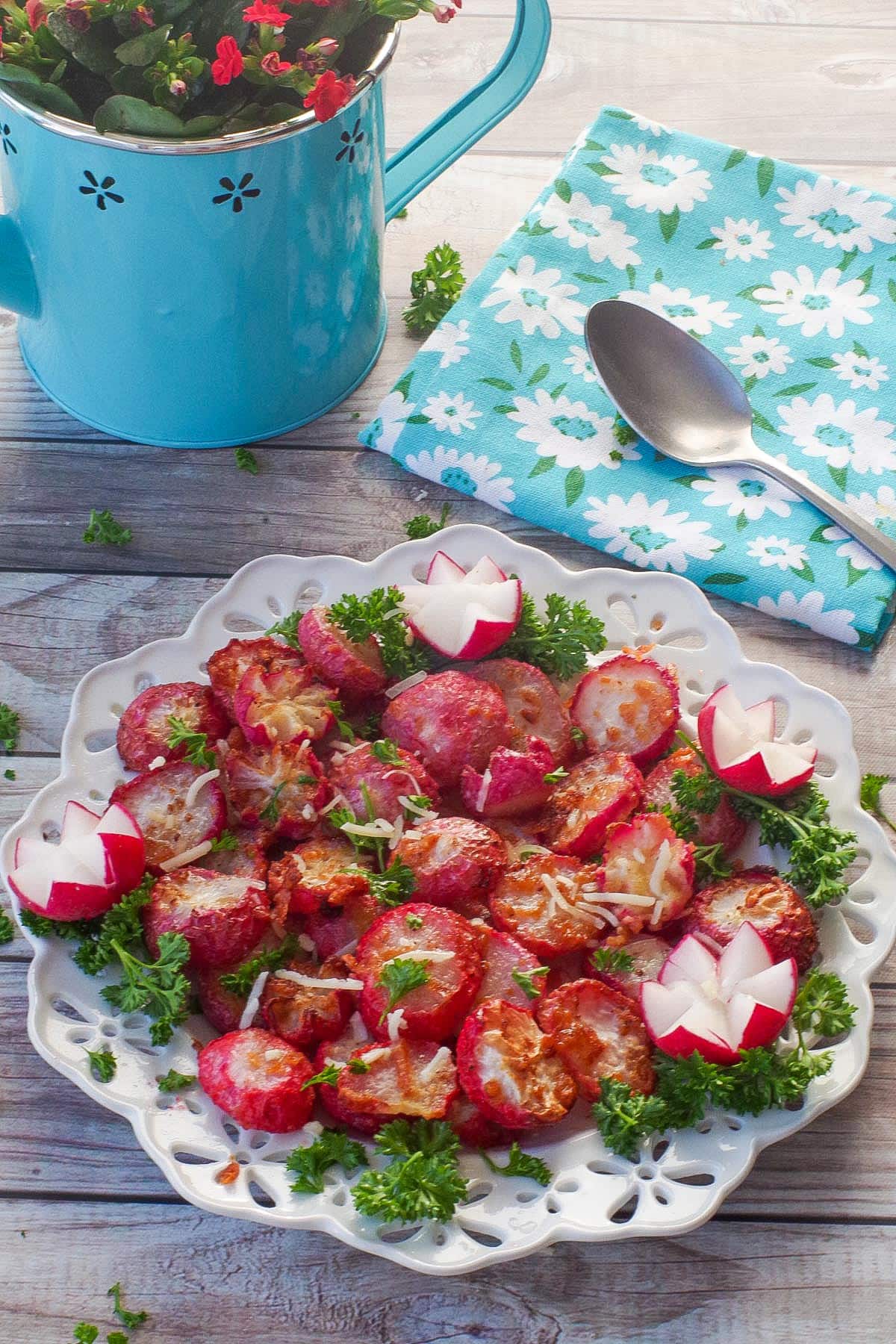 Air Fryer roasted radishes on a white plate with a watering can flower pot in the background and a tea towel with a spoon on it.