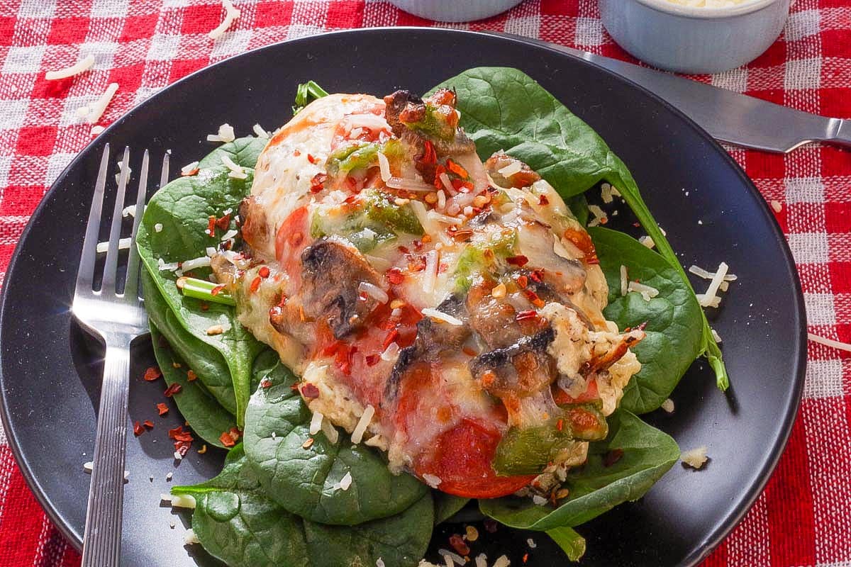 A piece of Healthy Pizza chicken with white sauce on a bed of lettuce on a black plate.