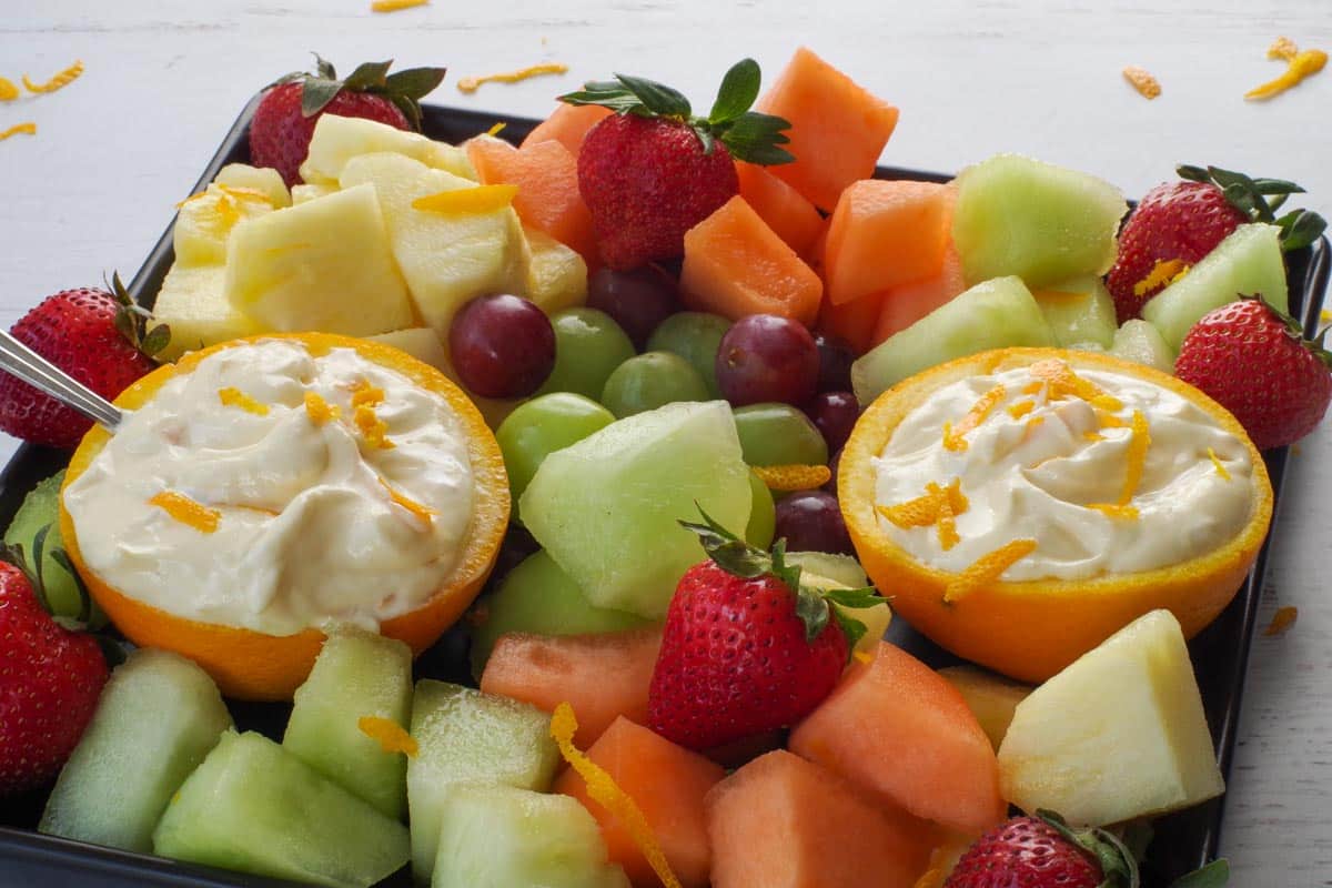 Orange Creamsicle Dip in hollowed out orange halves on a black tray with a variety of fruit.