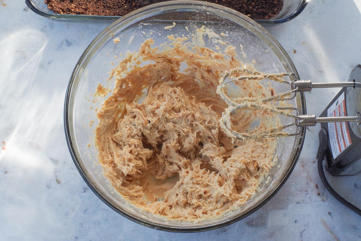 Cream cheese mixture beaten together in  glass bowl with beaters over the bowl.