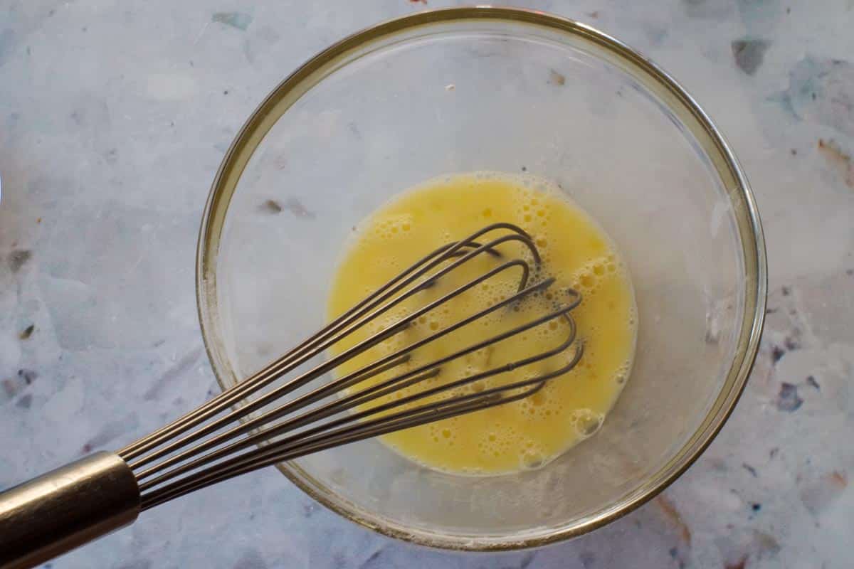 Egg being whisked with whisk in glass bowl.