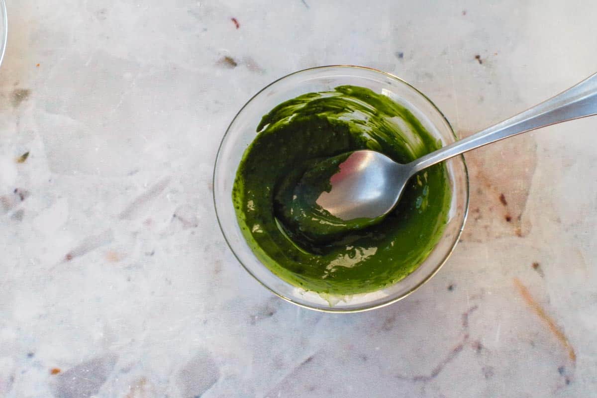 Matcha mixed with a little water to make a paste in a small glass bowl, with a spoon.