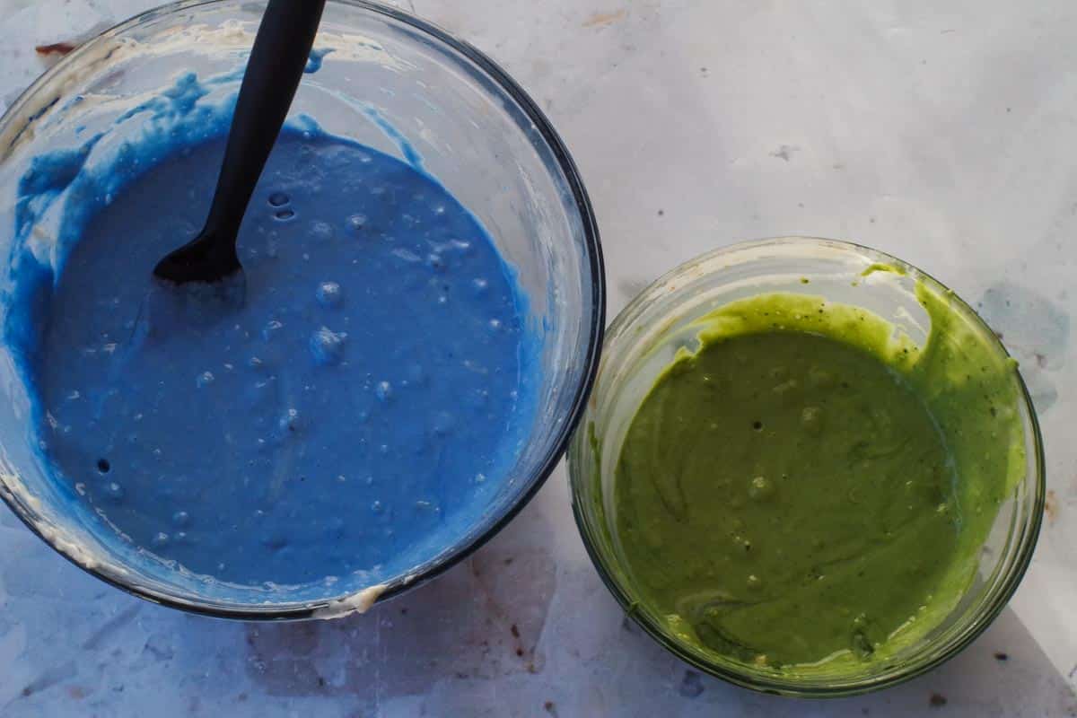 Blue batter in large glass bowl and green batter in smaller glass bowl.