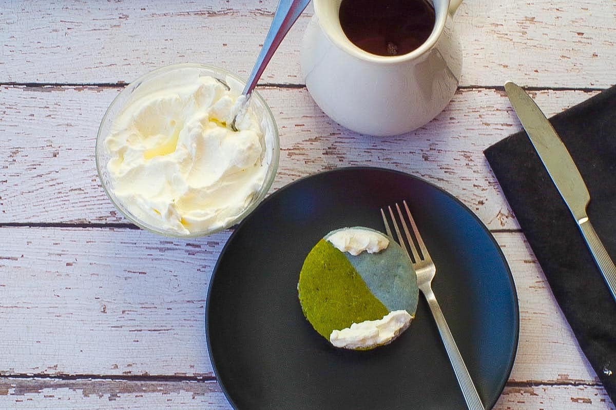 Sheet Pan Easy Earth Day Pancake cut into a round globe on a black plate with whipped cream and syrup in the background.