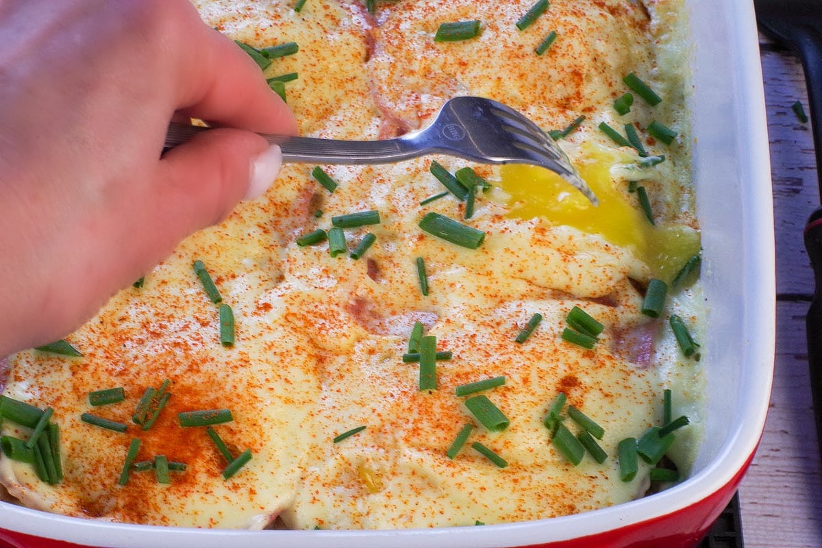 Fork poking egg yolks in Eggs Benedict Casserole.
