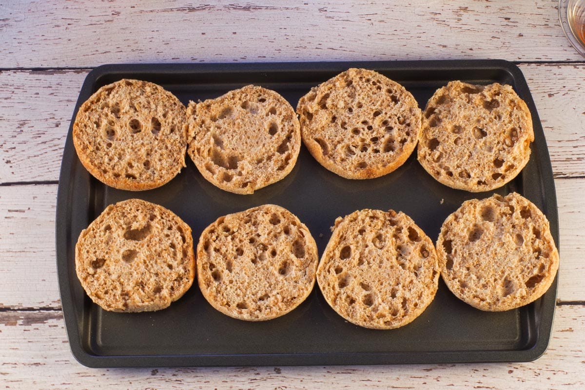 8 sliced English muffins on a baking sheet with the cut side facing up.