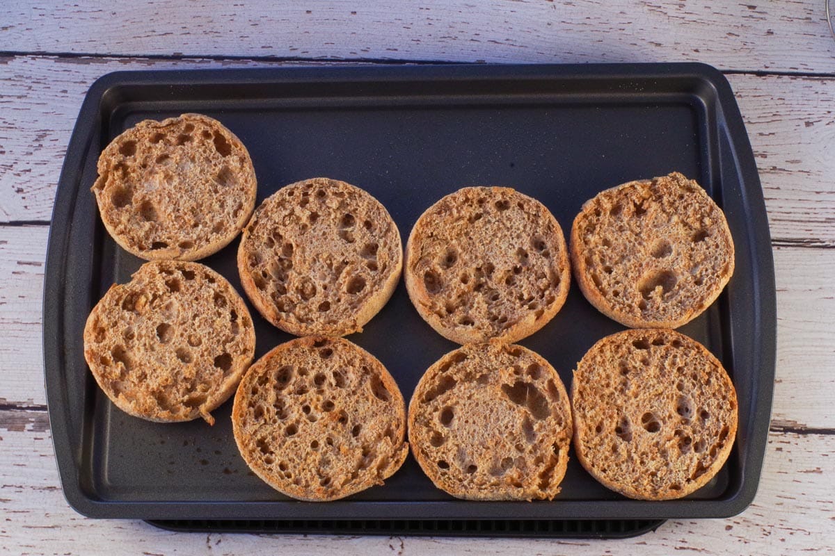 Toasted English muffin halves on a baking sheet,