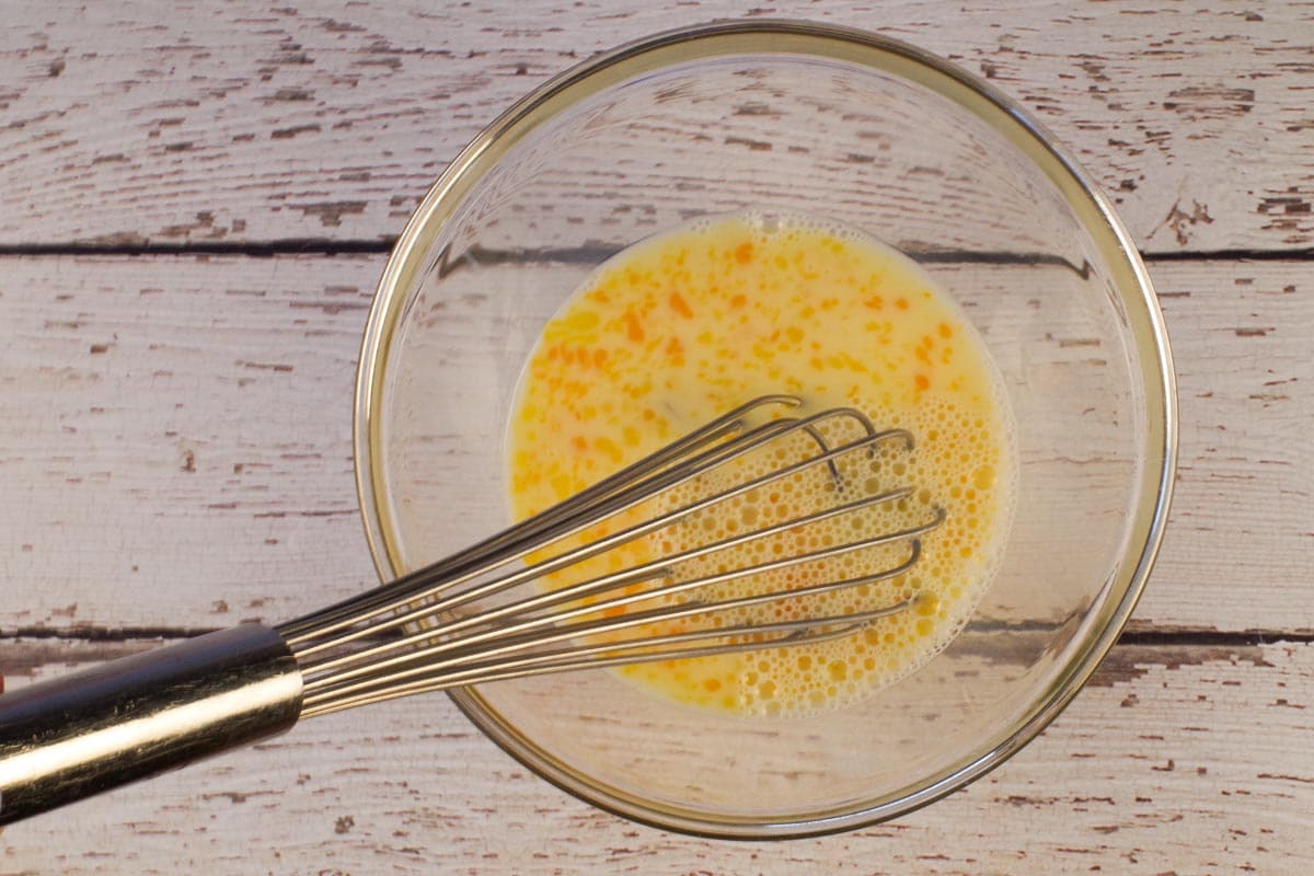 2 Eggs and milk whisked together in glass bowl with metal whisk.