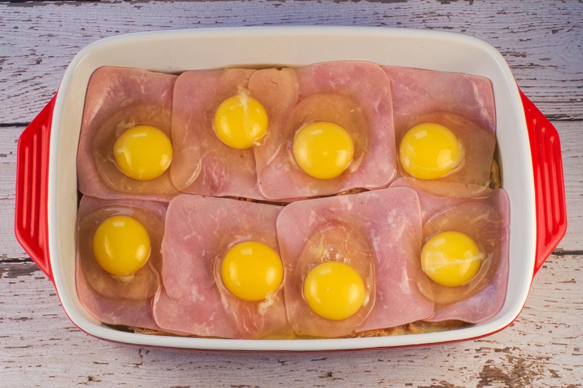 Eggs cracked on top of ham slices in casserole dish.