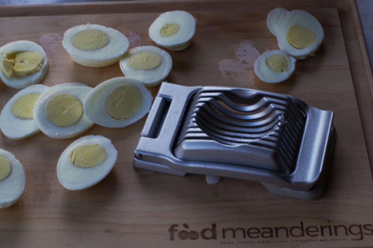 egg slicer and sliced eggs on a wooden cutting board.