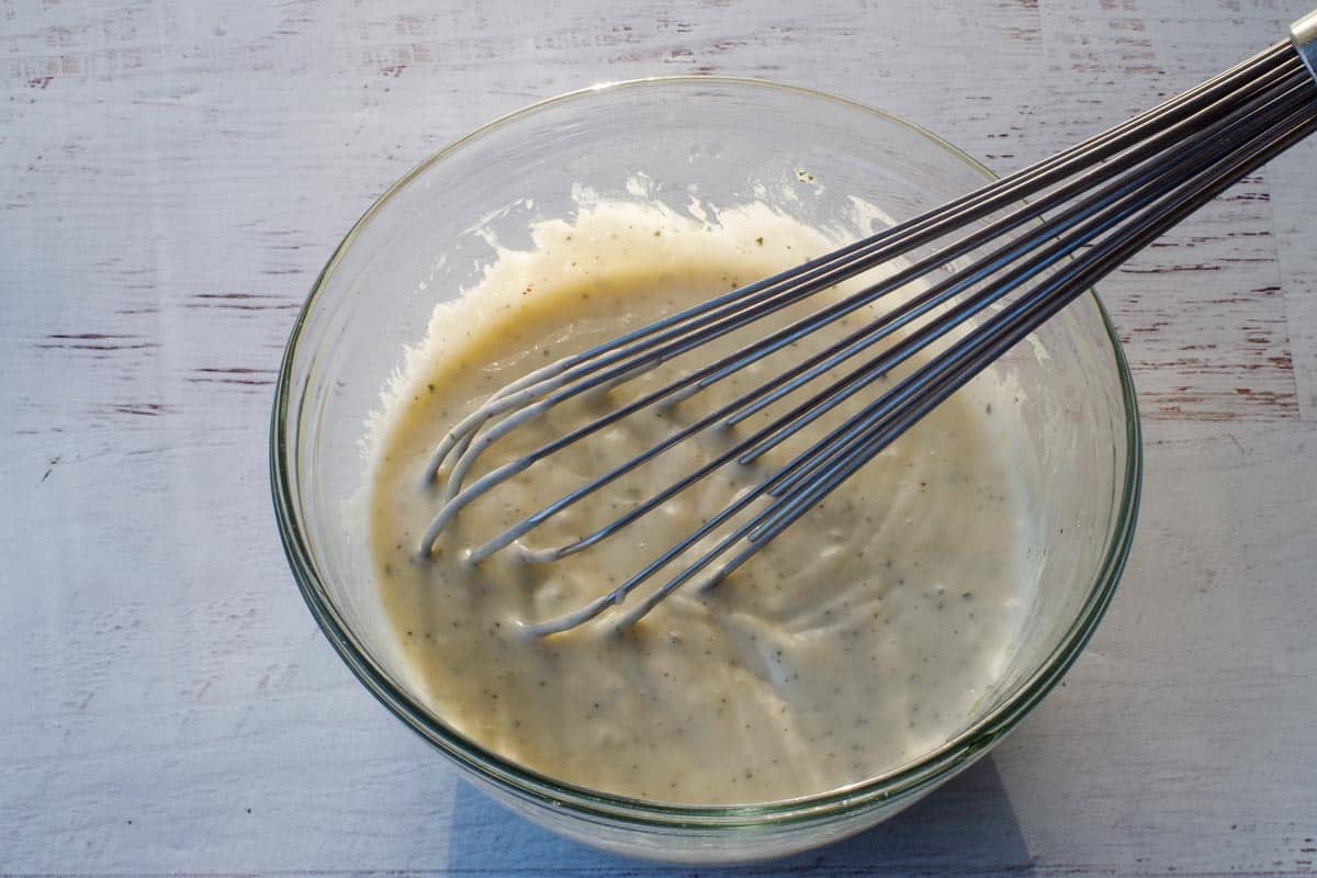 Salad dressing whisked together in a glass bowl with a large, metal whisk,