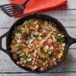 Mexican Street Corn Chicken in a cast iron pan with an orange napkin and a black spatula in the background.