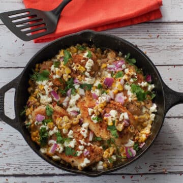 Mexican Street Corn Chicken in a cast iron pan with an orange napkin and a black spatula in the background.