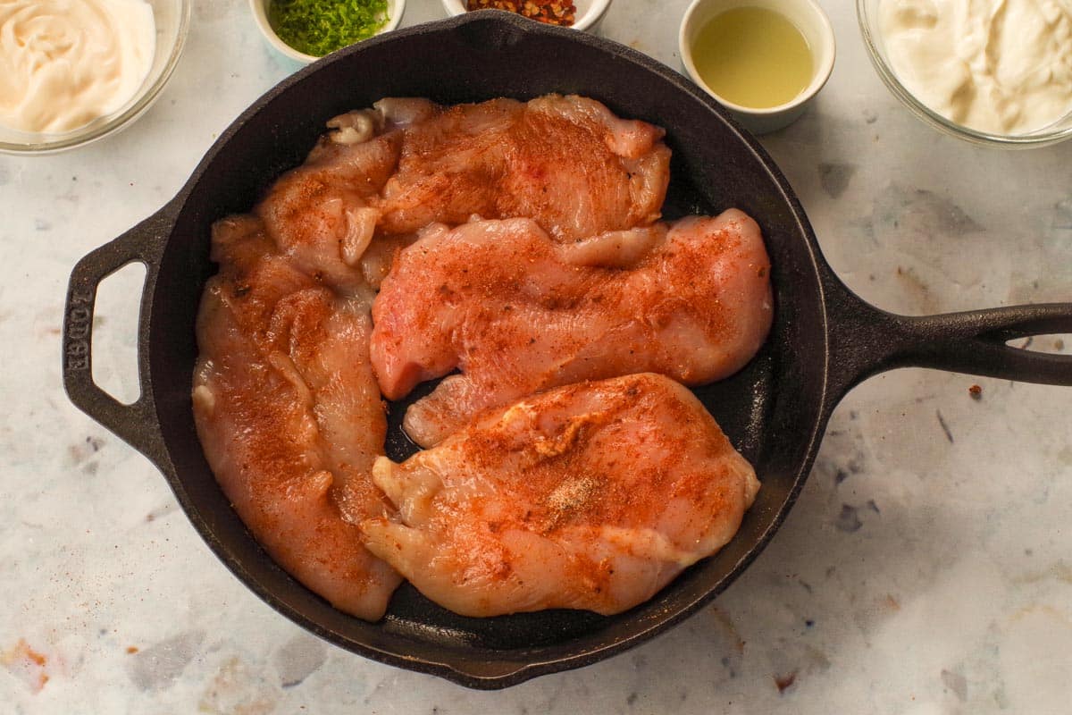 4 pieces of raw chicken breast with rub in a cast-iron frying pan.
