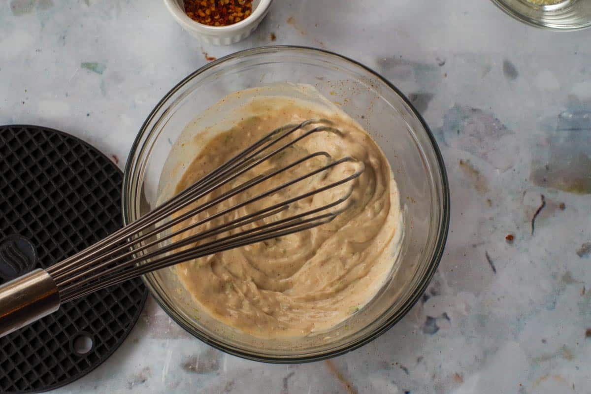 Sauce whisked together in medium glass bowl with large metal whisk.