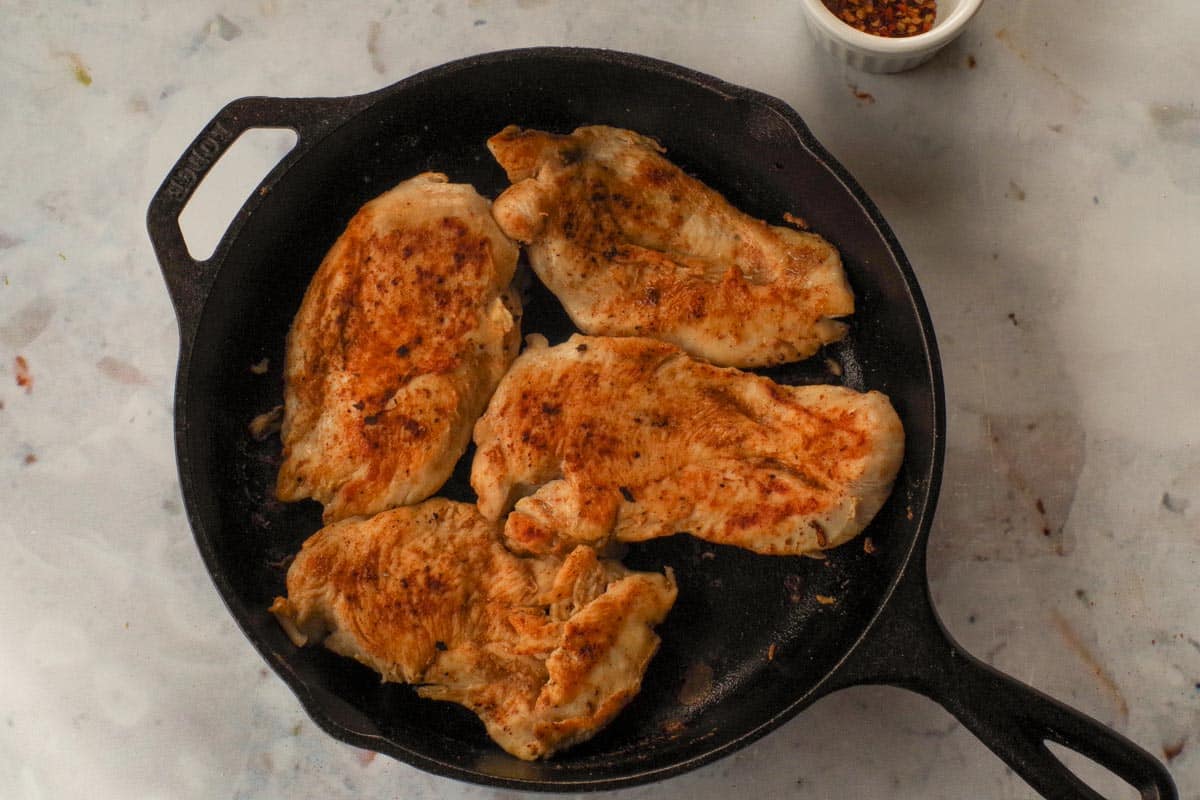 4 pieces of cooked chicken in cast iron frying pan.