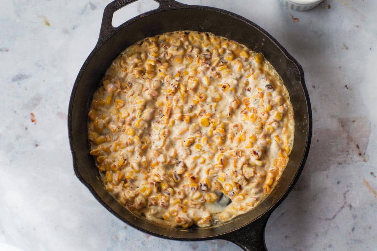 Sauce mixed into corn in cast-iron frying pan.