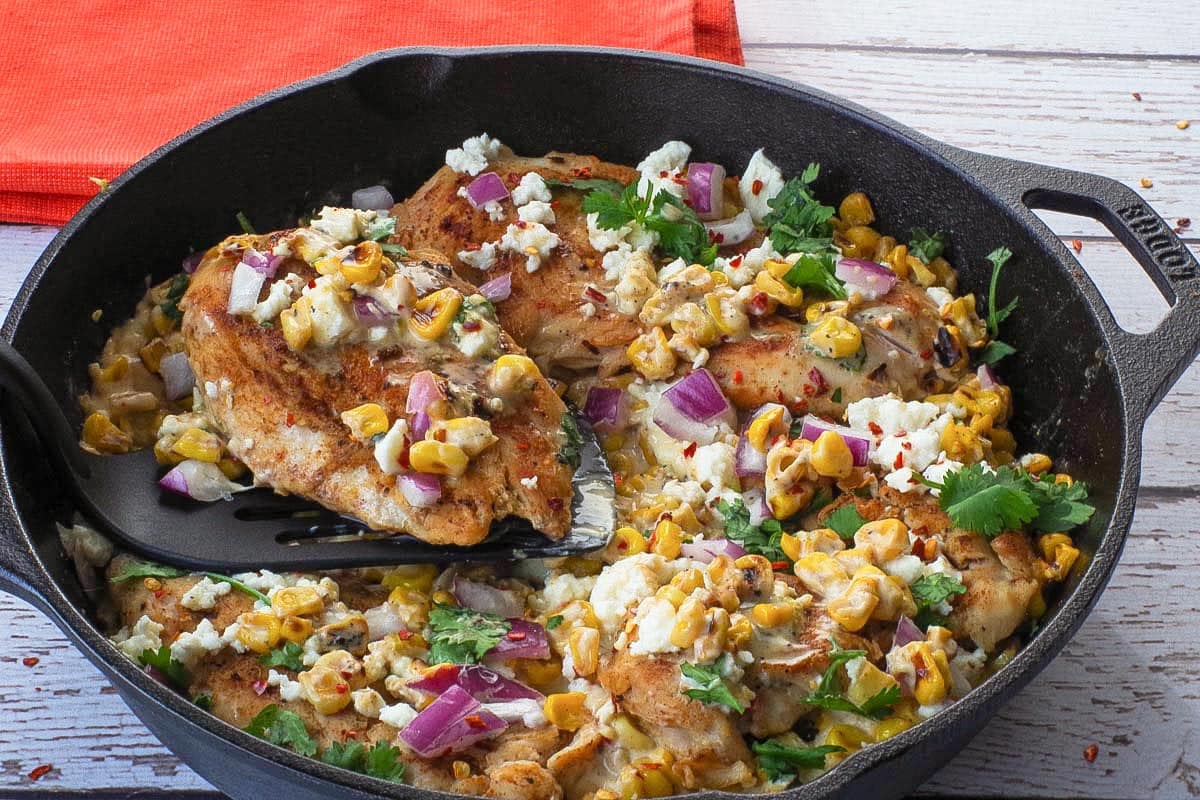 Mexcan Street Corn Chicken in a cast iron pan with a piece being lifted out.