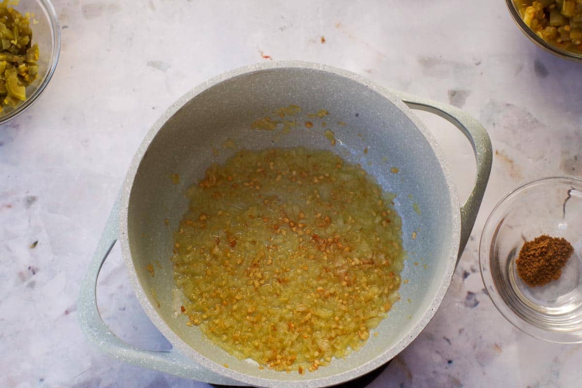 Garlic, onion and butter being cooked in a blue pot for New Mexican Chile Con Queso Dip.