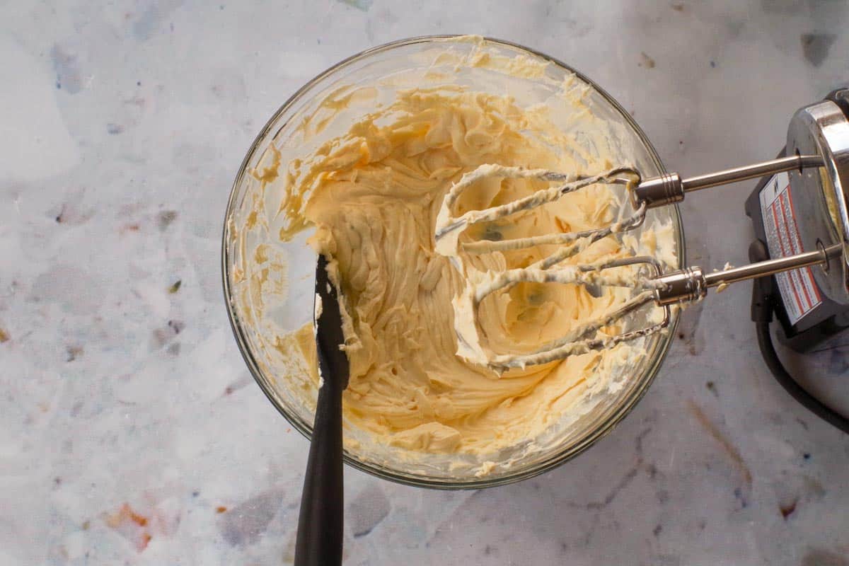 Cream cheese and concentrated orange juice beaten together in a glass bowl, with beaters over the bowl.