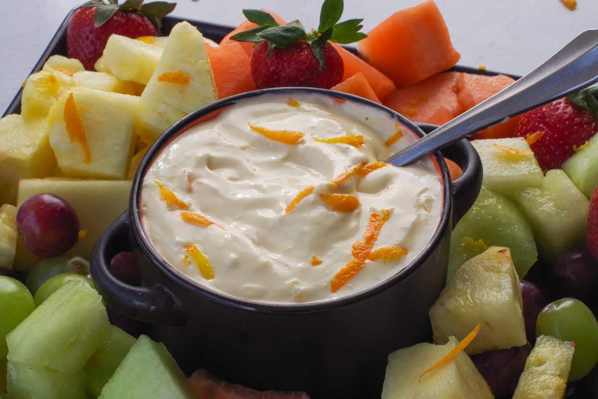 Orange Creamsicle Dip in a black bowl, surrounded by fruit on a black tray.
