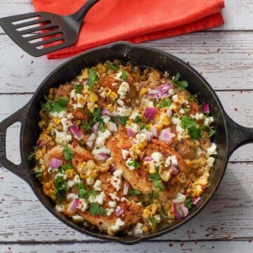 One-Pan Mexican Street Corn Chicken in a cast iron pan with an orange napkin and black spatula in the background.